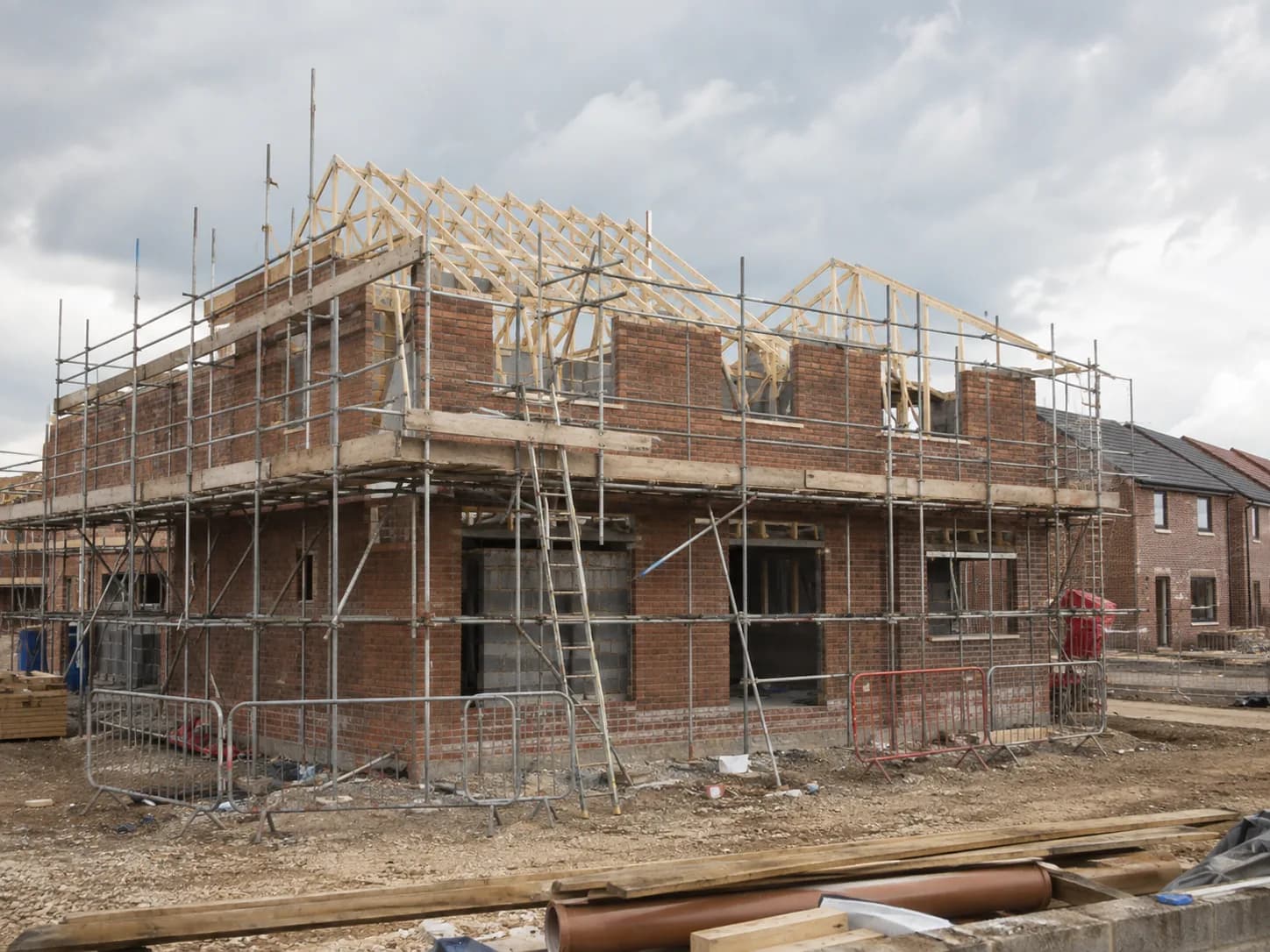 A British residential scheme mid-build, brick shell with scaffolding and exposed roof trusses